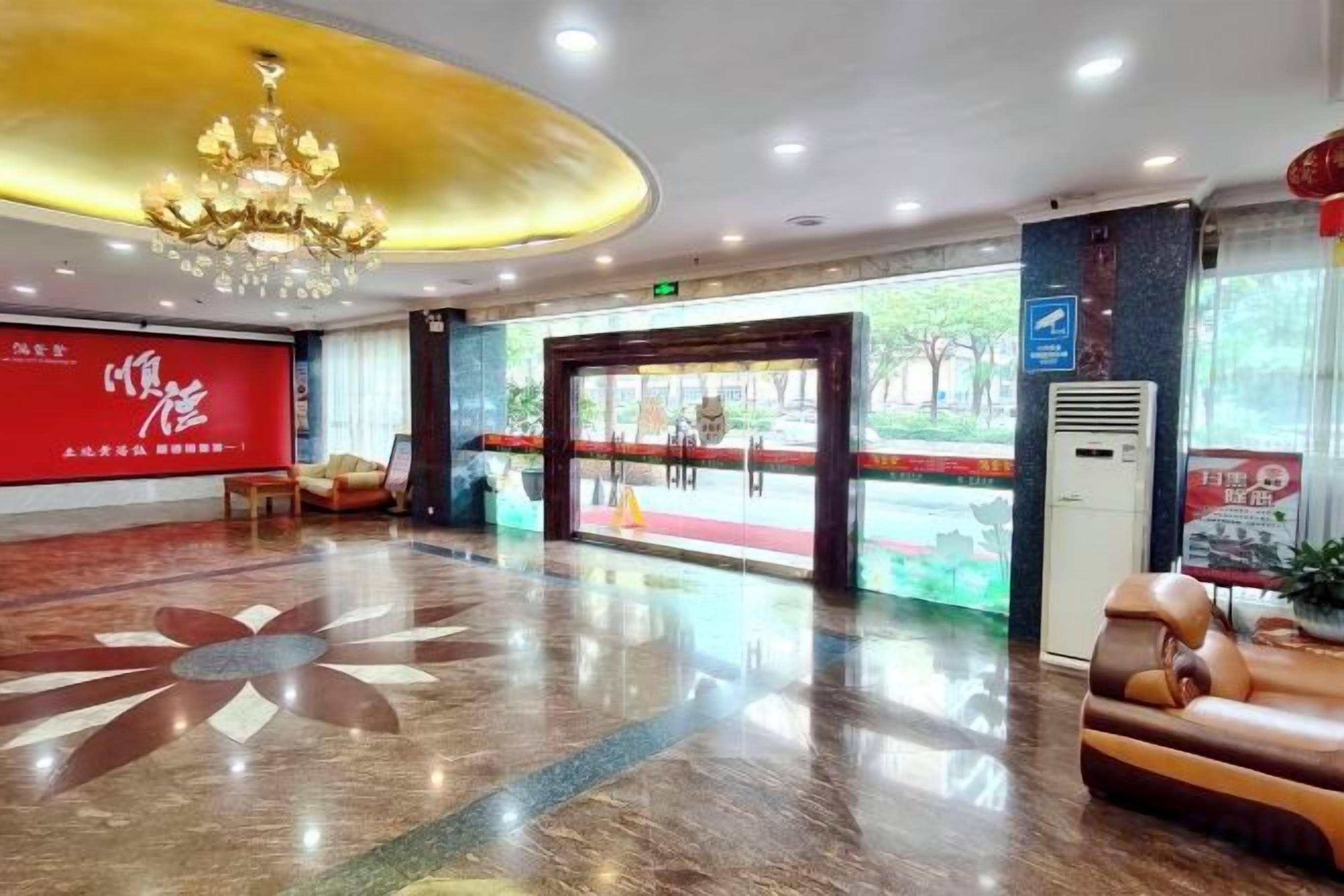 Un vestíbulo de hotel con una pared roja, una lámpara de araña, una mesa de recepción y un ventanal grande.