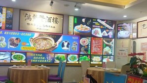 L’intérieur d’un restaurant, avec de nombreuses tables, des chaises et un mur où sont exposés différents plats et leurs prix.