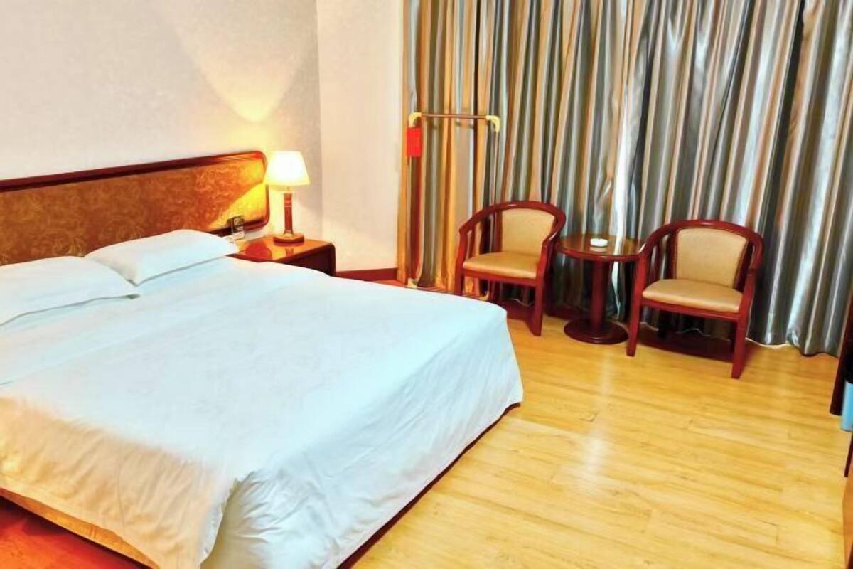 A hotel room with a bed, a nightstand, a lamp, two chairs, and a curtain.