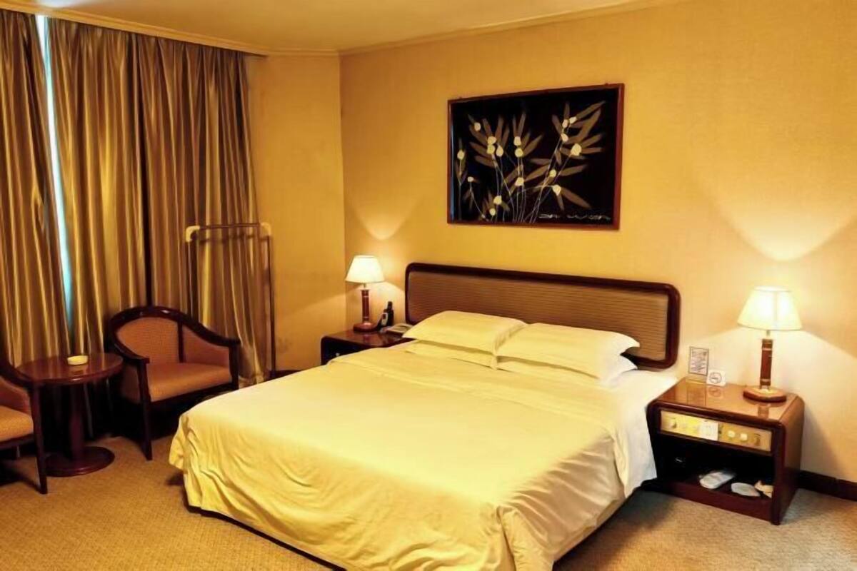 A hotel room with a bed, two bedside tables, a chair, a lamp, and a painting on the wall.