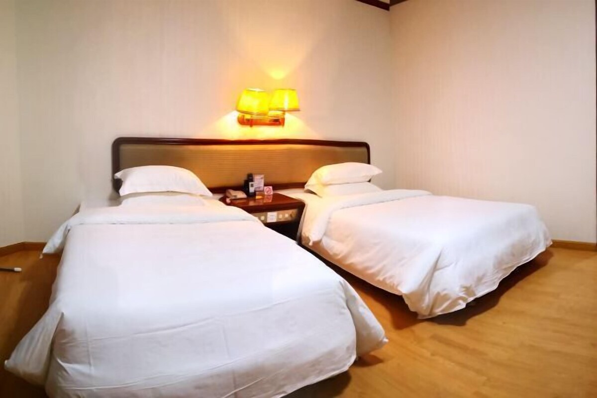 A hotel room with two single beds, a nightstand with a lamp, and a wooden floor.