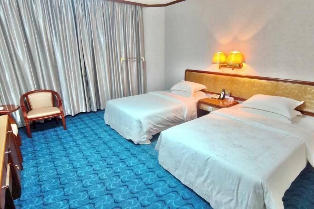 A hotel room with two beds, a chair, a desk, and a lamp.