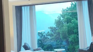 Una habitación con un ventanal grande, una cama, una silla y una mesita redonda.