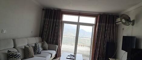 A living room with a sofa, a coffee table, a TV, and a balcony with curtains.