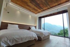 A bedroom with two beds, a wooden ceiling, and a large window with a mountain view.