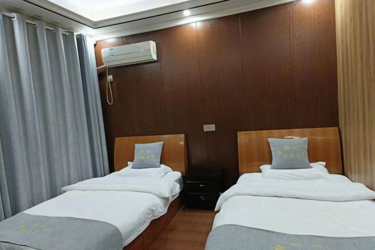 Habitación de hotel con dos camas, cabeceros de madera, mesitas de noche pequeñas y un equipo de aire acondicionado en la pared.