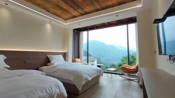 Una habitación de hotel moderna con dos camas, techo de madera, ventanas grandes y vistas a montañas.