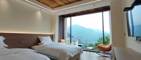 Een moderne hotelkamer met twee bedden, een houten plafond, grote ramen en uitzicht op bergen.