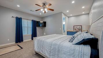 A bedroom with a bed, ceiling fan, TV, and a bathroom visible through an open door.