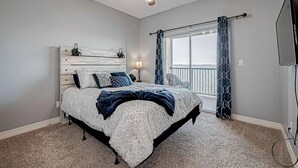 Une chambre avec un lit, un ventilateur de plafond, une fenêtre avec des rideaux et un téléviseur.