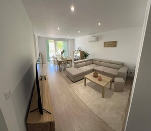 Ein modernes Wohnzimmer mit einer Eckcouch, einem Couchtisch und einem Essbereich mit Stühlen und einem Tisch.