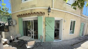 A building with a patio area featuring a table and chairs, a sliding door, and a small kitchen visible inside.
