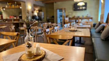 Een gezellig restaurantinterieur met houten tafels en stoelen, een houten plafond en een aan de muur bevestigde televisie.