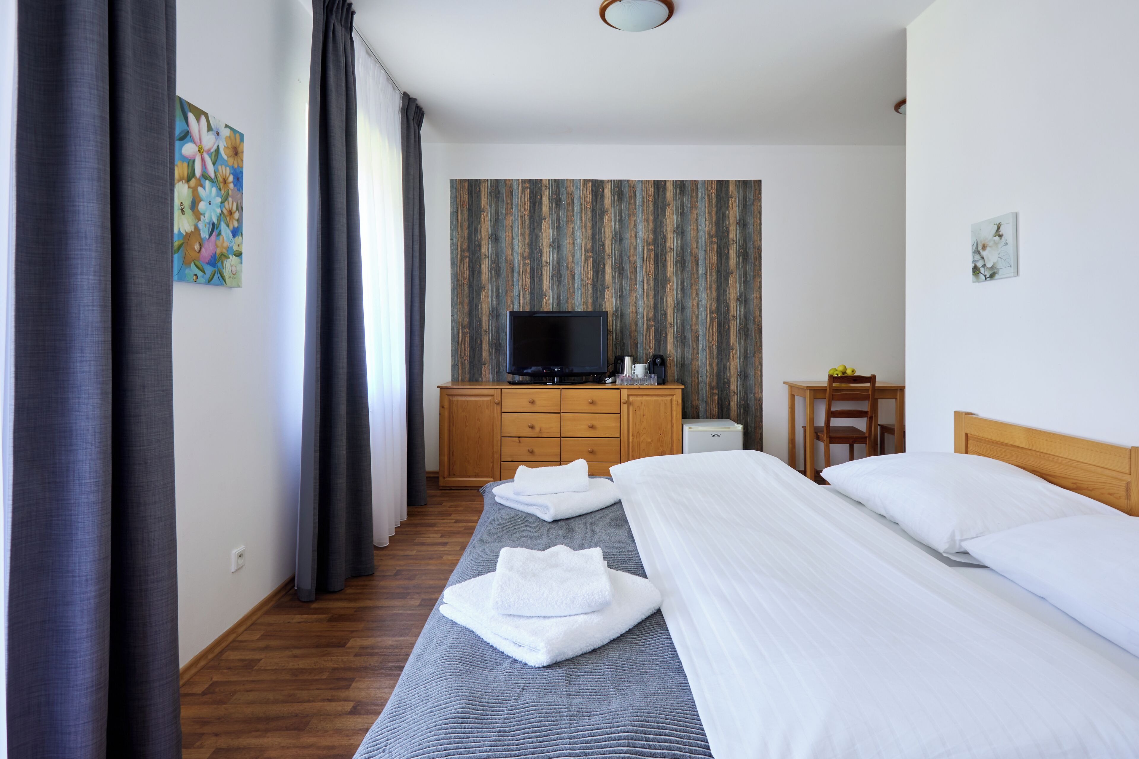 A hotel room with a bed, a TV, a wooden dresser, a desk, and a chair.