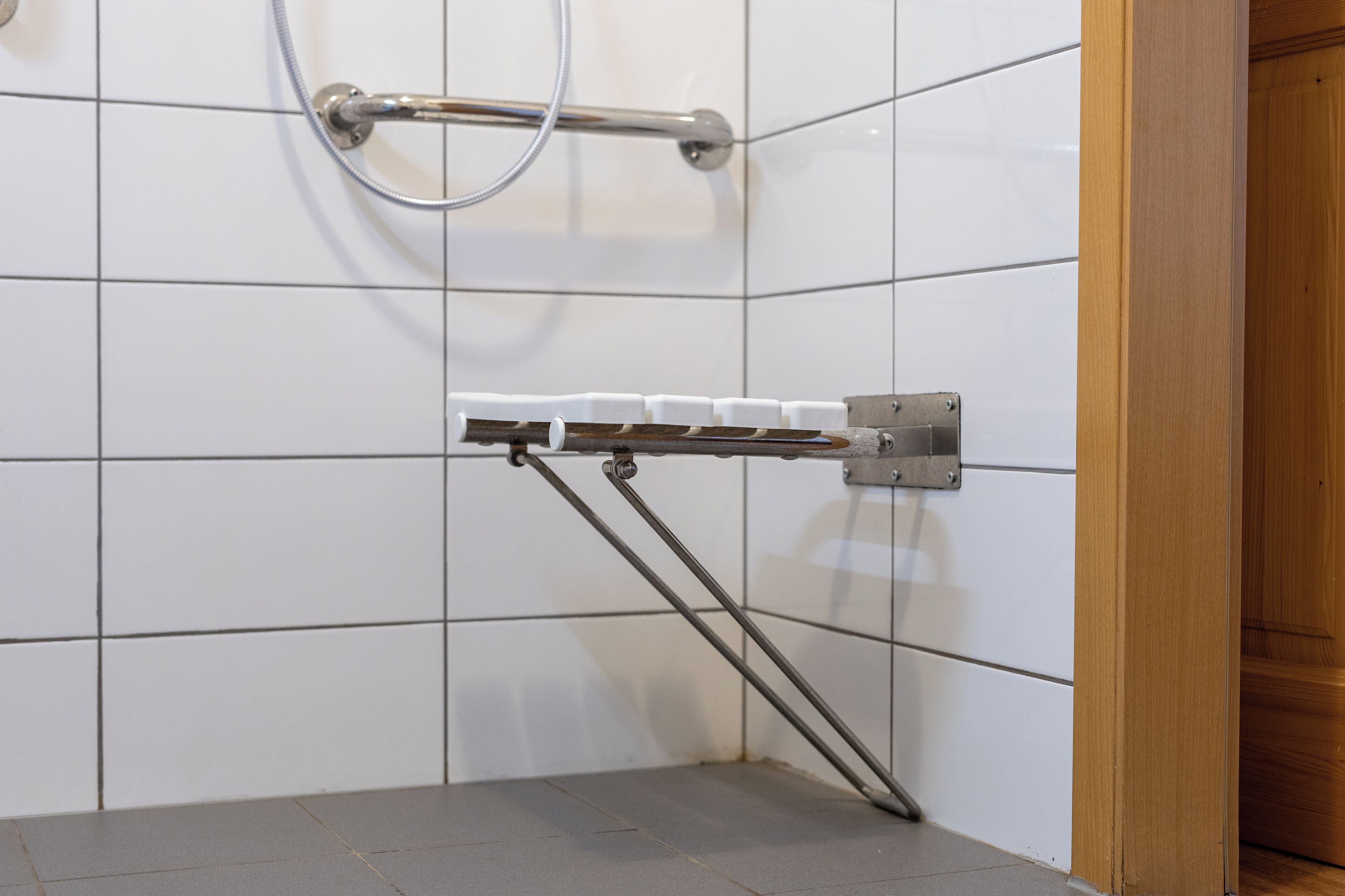 A bathroom with white tiled walls, a shower area with a glass door, and a towel rack with white towels.