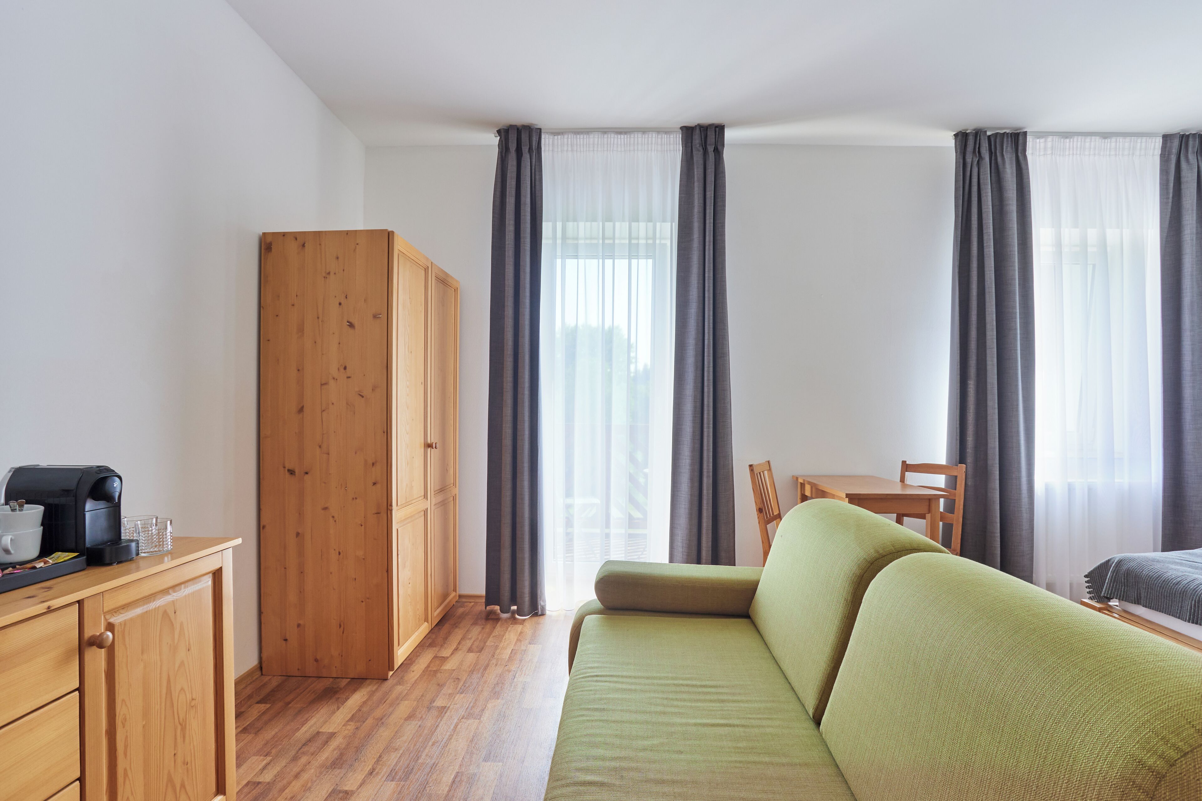 A room with a wooden wardrobe, a green sofa, a wooden table, and a chair.