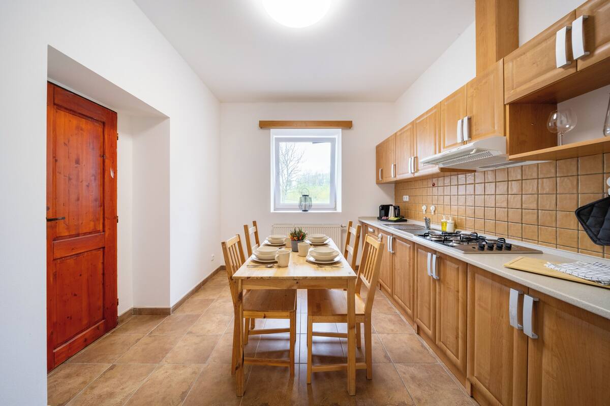 A kitchen with wooden cabinets, a tiled backsplash, a window, and a dining table set for four.