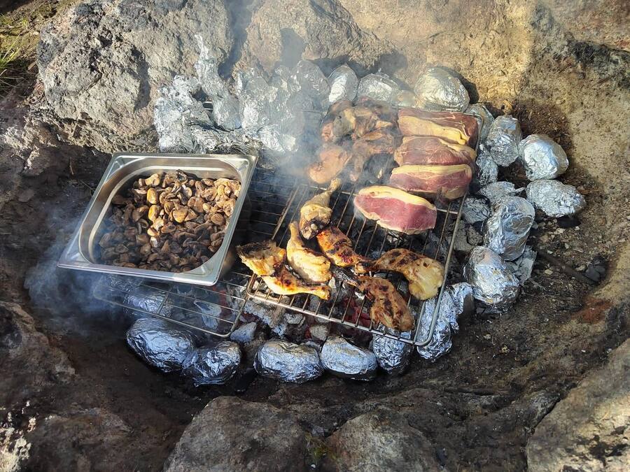 A barbecue with various meats and vegetables cooking over charcoal.