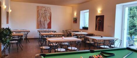 A billiards room with tables and chairs, a pool table, and artwork on the walls.