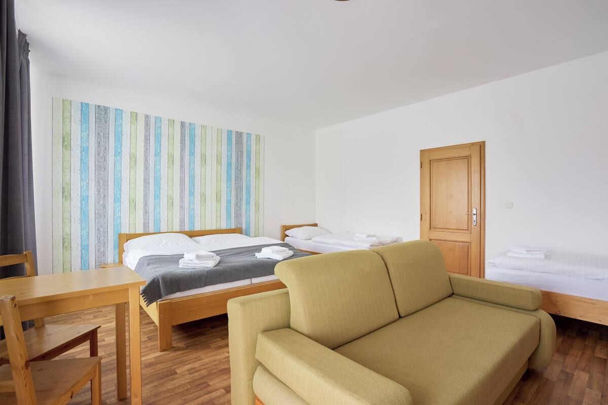 A hotel room with a bed, a sofa, a wooden table, and a door.
