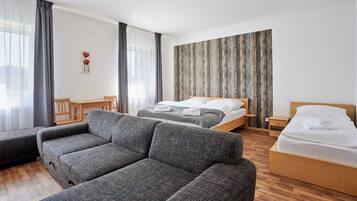 Una habitación de hotel moderna con un sofá gris, una cama de madera, una mesita de noche de madera y una silla de madera.