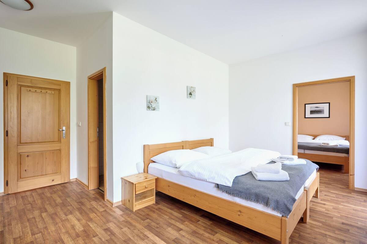 A bedroom with a wooden bed, a nightstand, a door, and a small wall-mounted shelf.