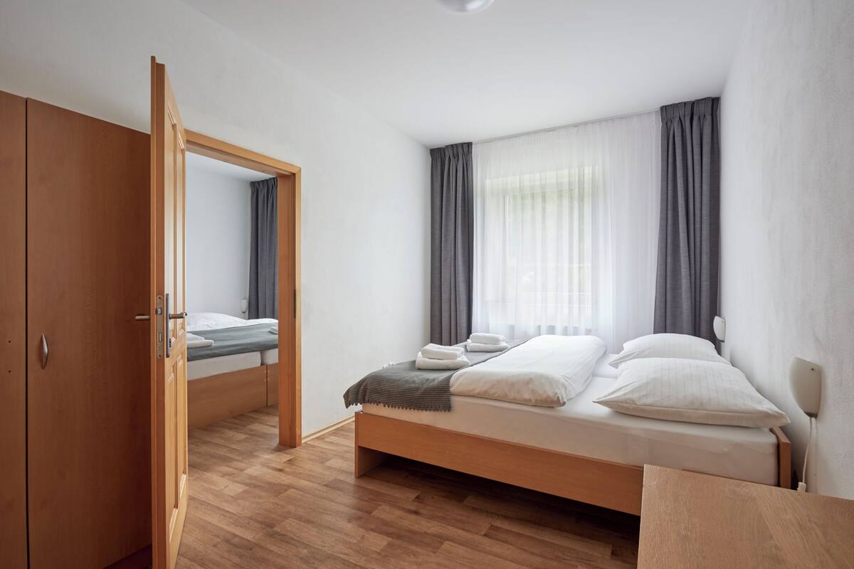A bedroom with a wooden bed, a wardrobe, a mirror, and a window with curtains.