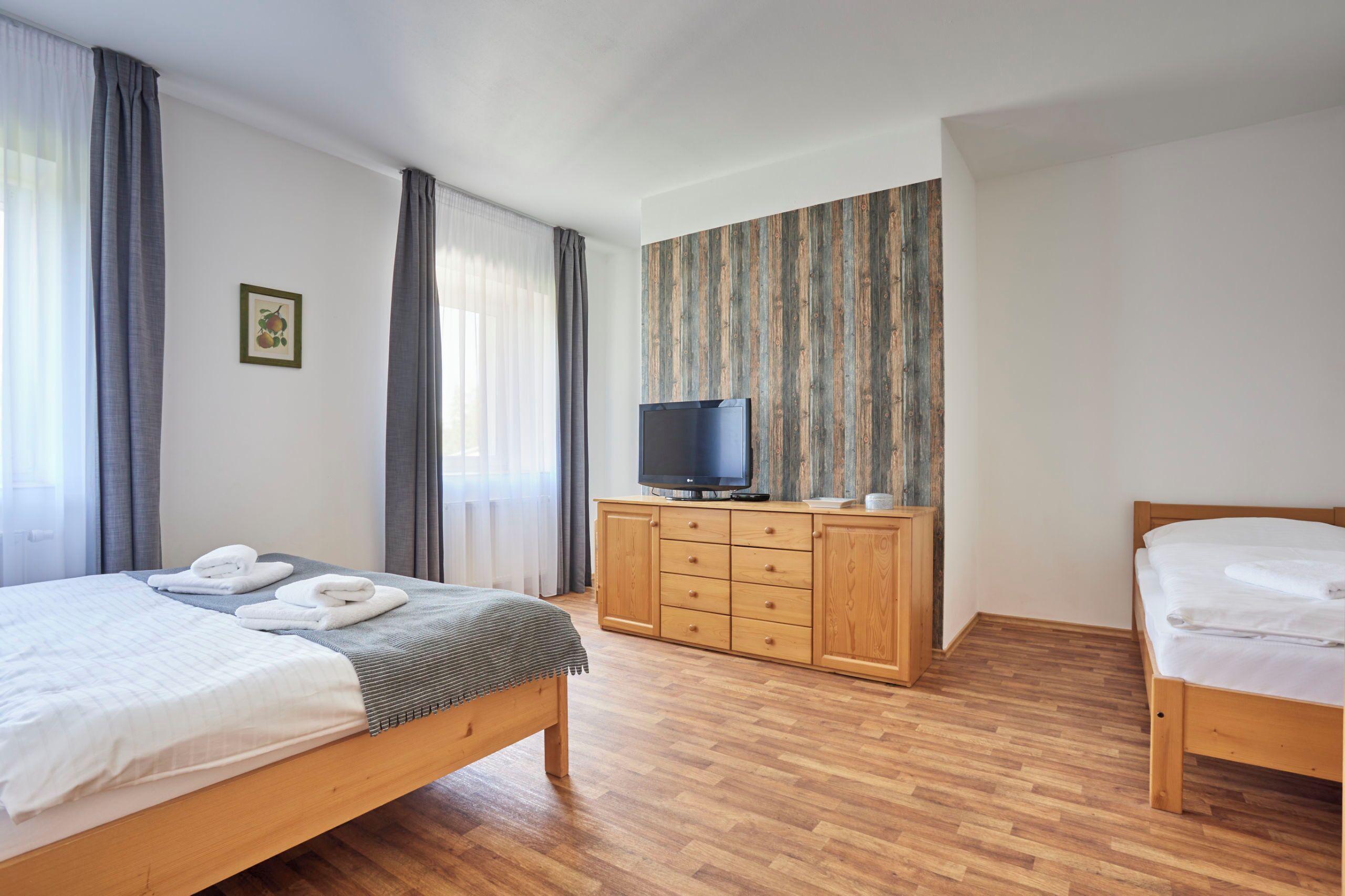 A hotel room with two beds, a wooden wardrobe, a television, and a window with curtains.