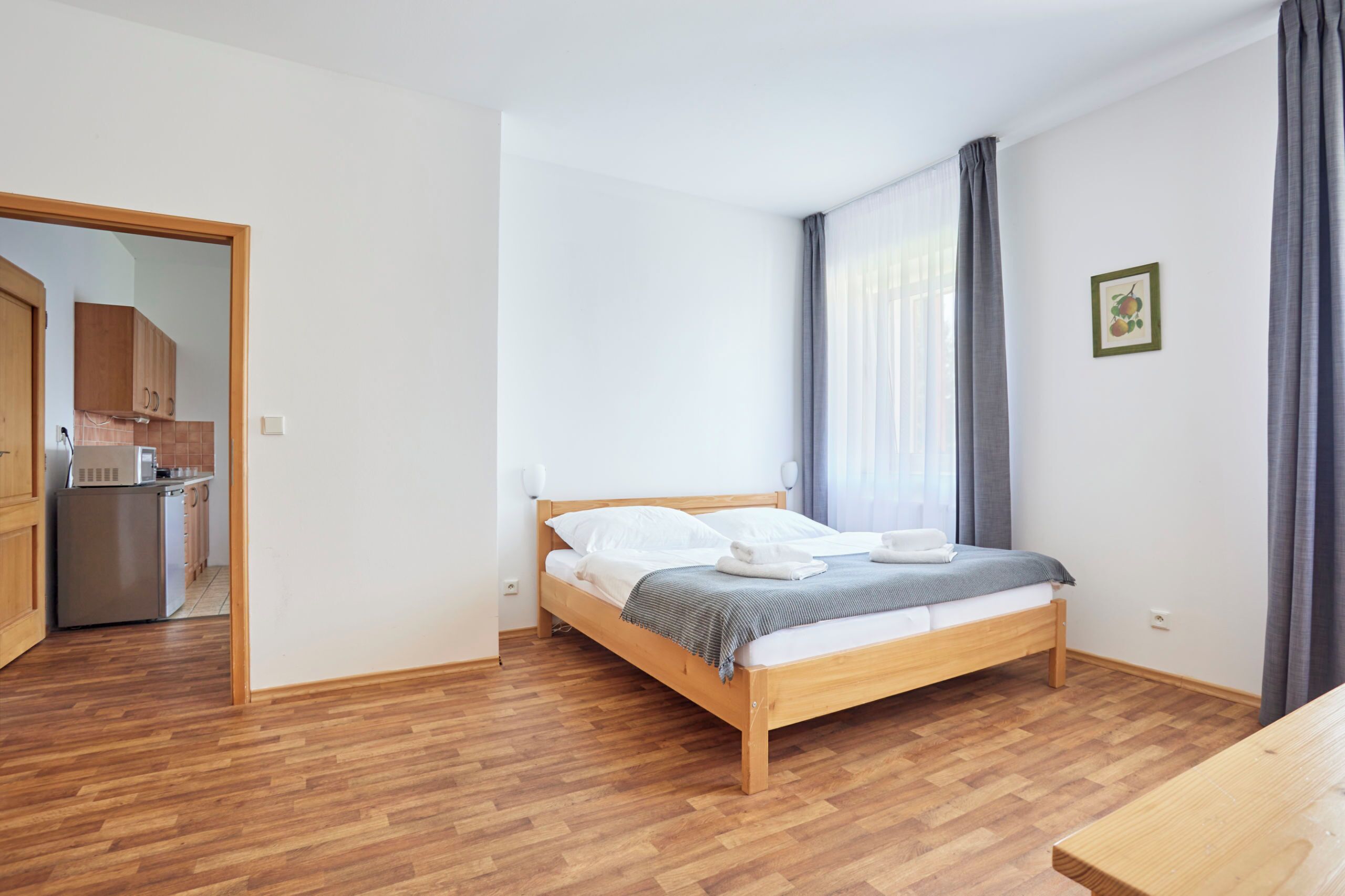 A bedroom with a wooden bed, a small kitchenette, and a wooden floor.