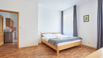 A bedroom with a wooden bed, a small kitchenette, and a wooden floor.