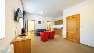 A spacious living area with a sofa, red ottomans, a wooden desk, and a television mounted on the wall.