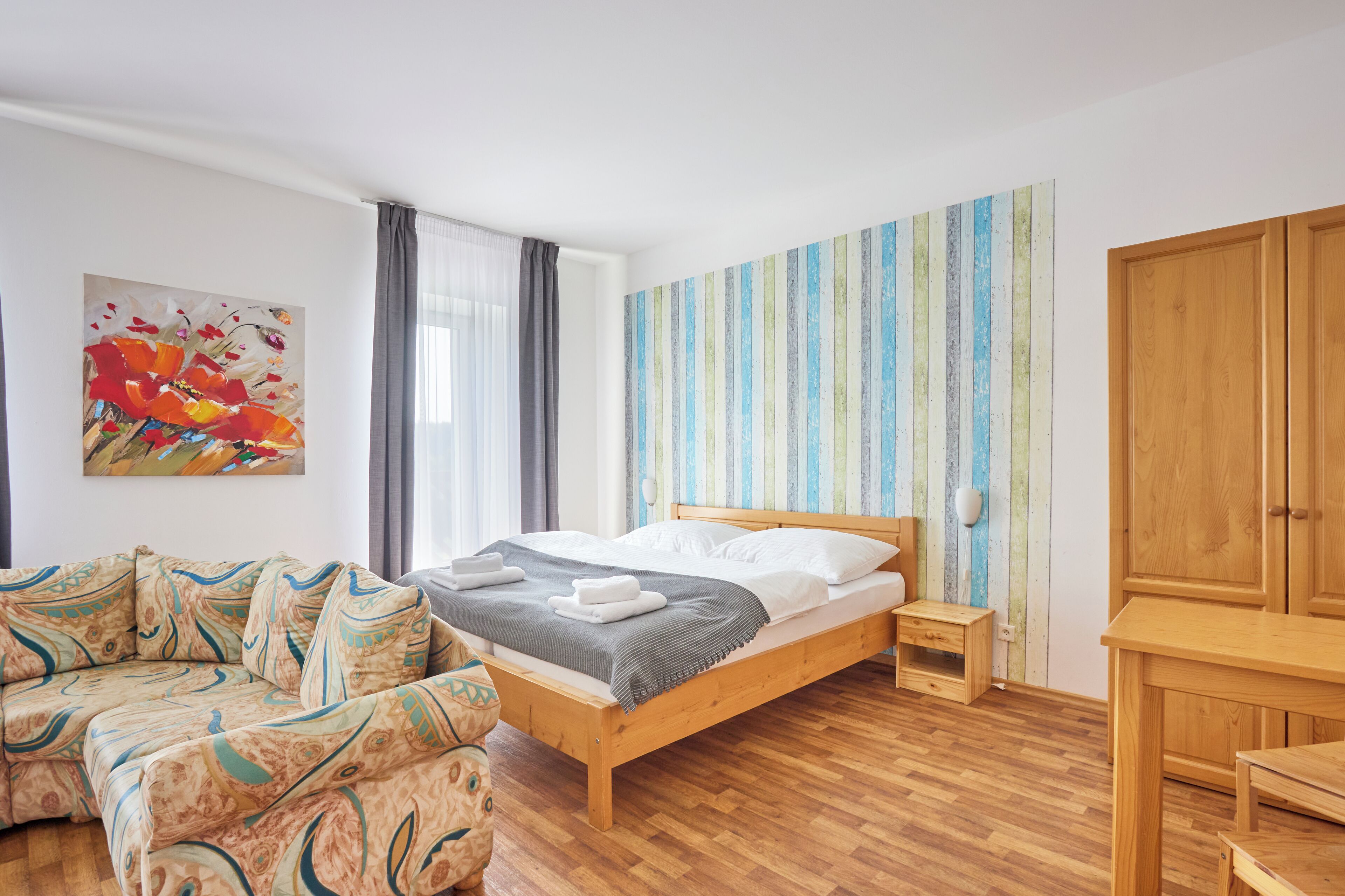 A bedroom with a wooden bed, a sofa, a wooden desk, and a colorful striped wall.