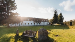 A building with a white exterior, a bench, and a large rock in a grassy area. - Resort Pasečná (Prední Výton)