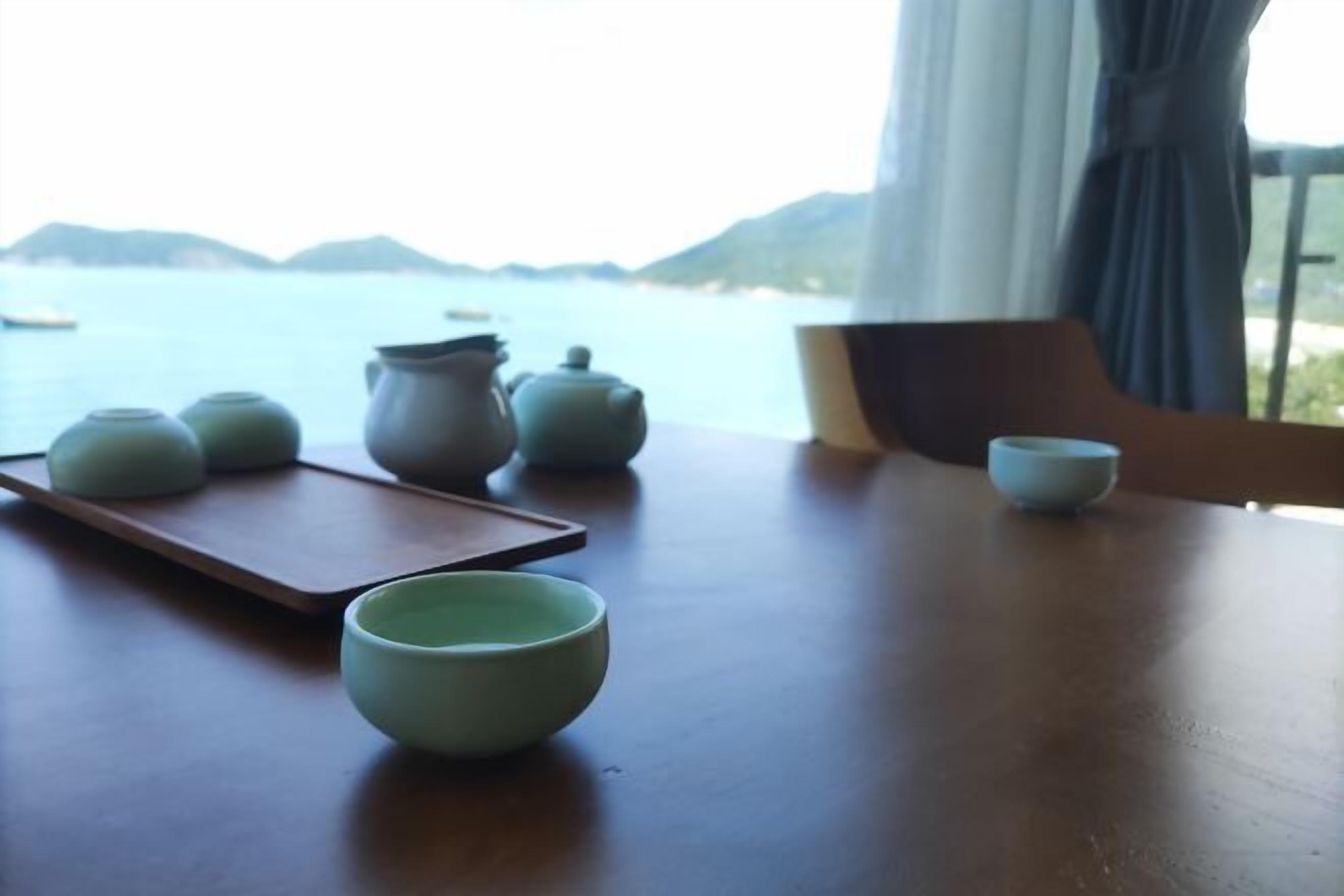 A table with teapots and cups, a tray, and a view of the sea and mountains.