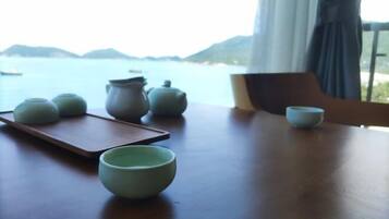 A table with teapots and cups, a tray, and a view of the sea and mountains.