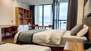 Habitación de hotel con dos camas, un escritorio y vista al mar.