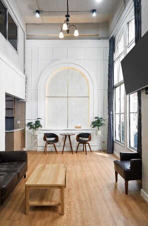 A spacious room with a large arched window, a wooden coffee table, two black chairs, a black sofa, and a television mounted on the wall. - G5 Hostel Bangkok (Bangkok)