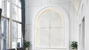 A spacious room with a large arched window, leather sofas, wooden tables, and potted plants. - G5 Hostel Bangkok (Bangkok)