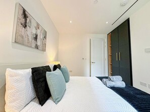 A modern bedroom with a large bed, a wardrobe, and a painting on the wall.