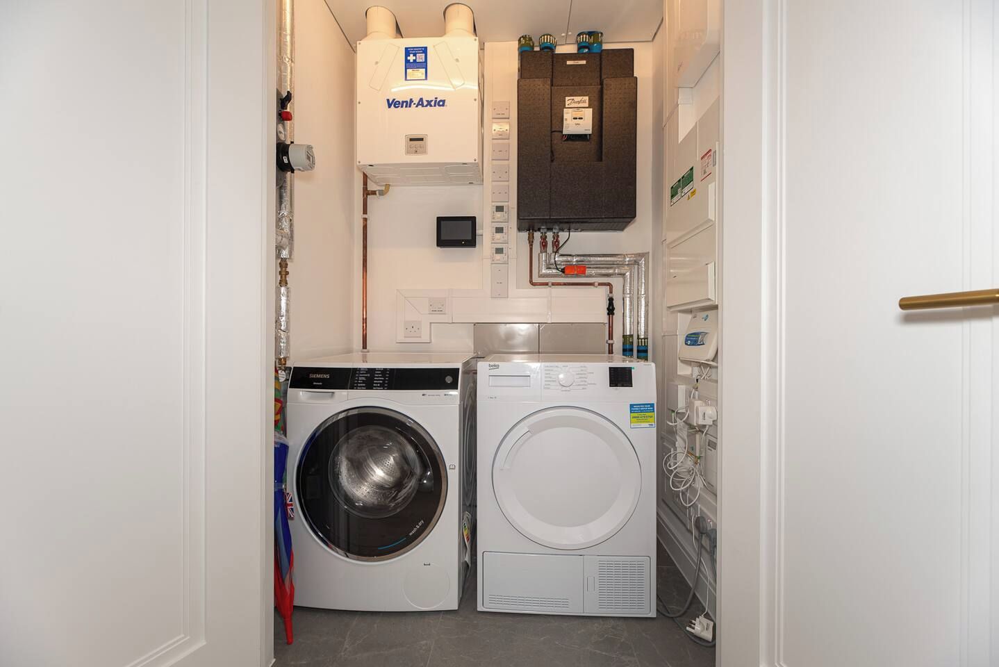 A laundry room with a Siemens washing machine, a white dryer, and a Vent-Axia water heater.