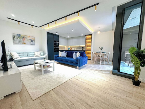 A modern living room with a blue sofa, white coffee table, and a flat-screen TV.