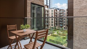 A balcony with a wooden table and chairs, a potted plant, and a view of a residential building complex. - Farringdon Lux 2-bed flat w. Balcony - Clerkenwell (London)