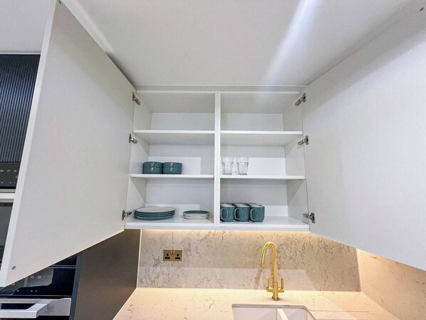 A kitchen with a built-in sink, white cabinets, and shelves with dishes and cups.