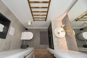 A modern bathroom with a white toilet, a sink with gold fixtures, and a mirror.