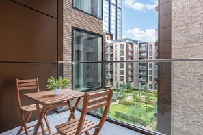 A balcony with a wooden table and chairs, a potted plant, and a view of a residential building complex.