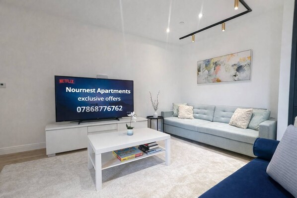 A modern living room with a flat-screen TV, a sofa, a coffee table, and a painting on the wall.