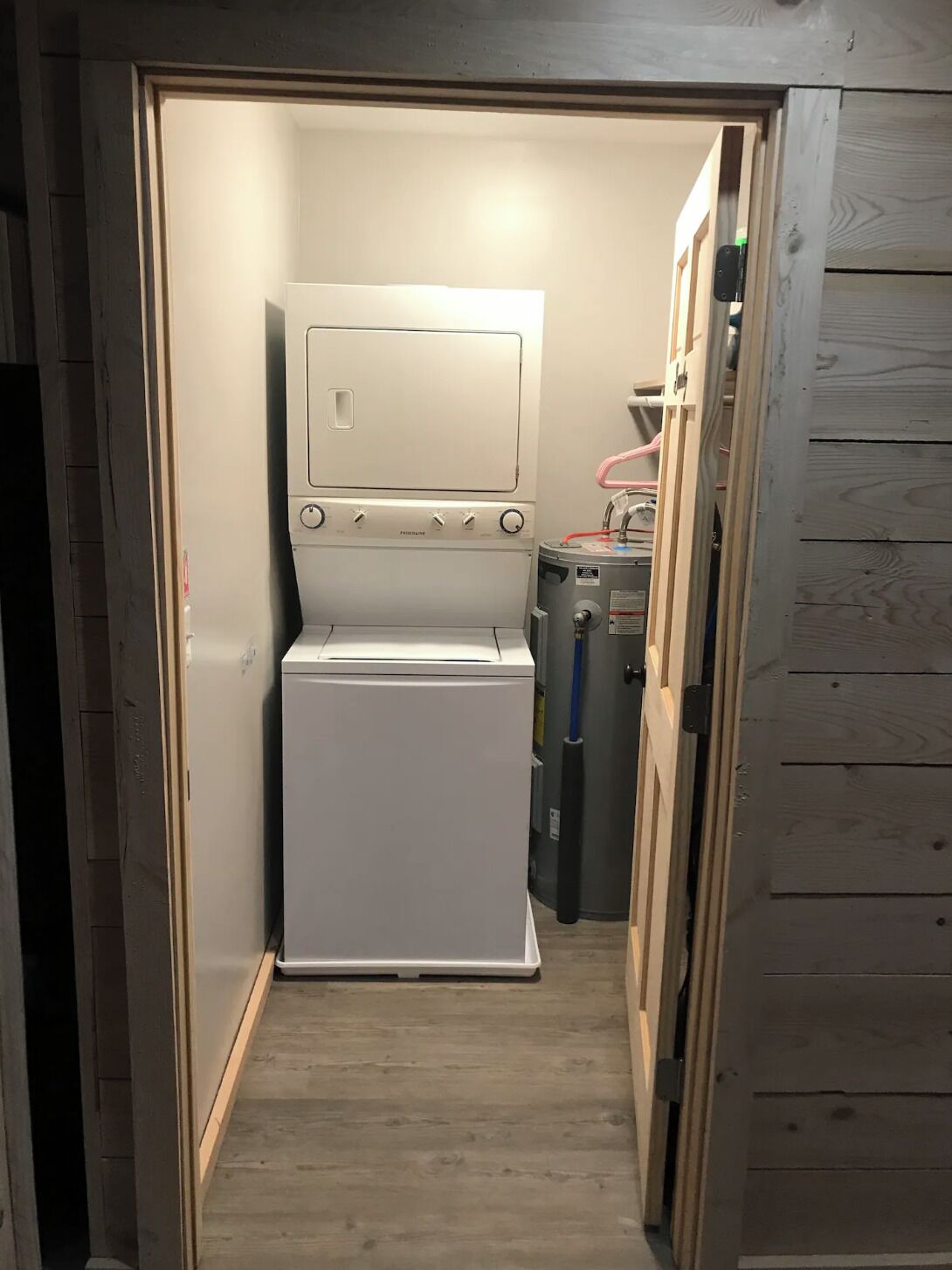 Ein kleiner, gut beleuchteter Waschraum mit einer weißen Waschmaschine und einem Trockner, einem Warmwasserbereiter und einer Holztür.