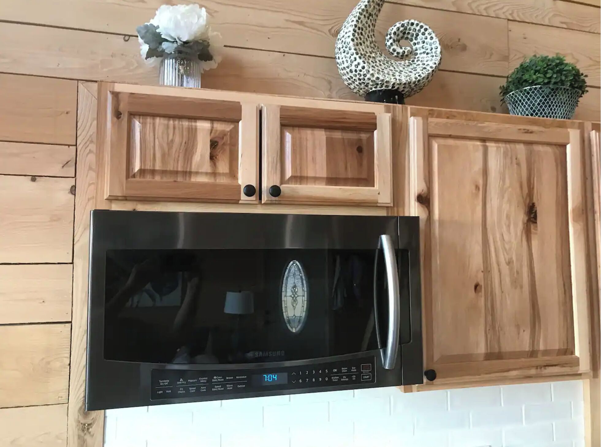 A kitchen with wooden cabinets, a stainless steel microwave, and a clock displaying 7:04.