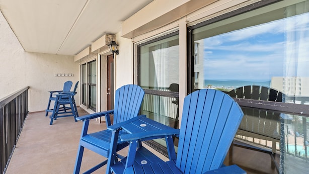 Un balcón con sillas Adirondack azules, una pequeña mesa y vista al océano.