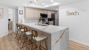 Una cocina moderna con una isla de mármol, taburetes de bar y un letrero en la pared que dice 'Beach'.